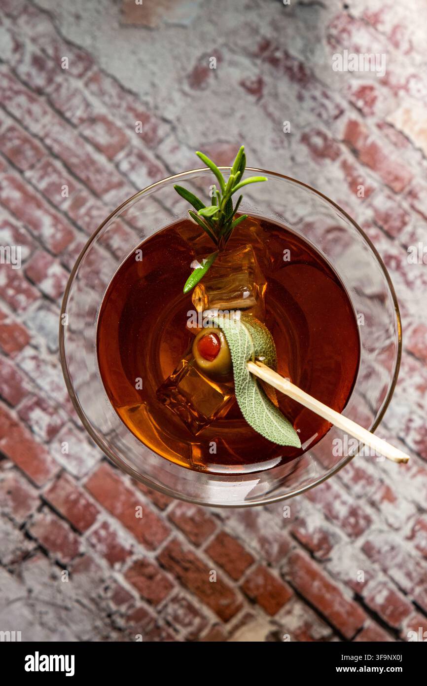 un cocktail cool pour la célébration avec de la sauge, du romarin et de l'olive sur une table avec des briques. Banque D'Images