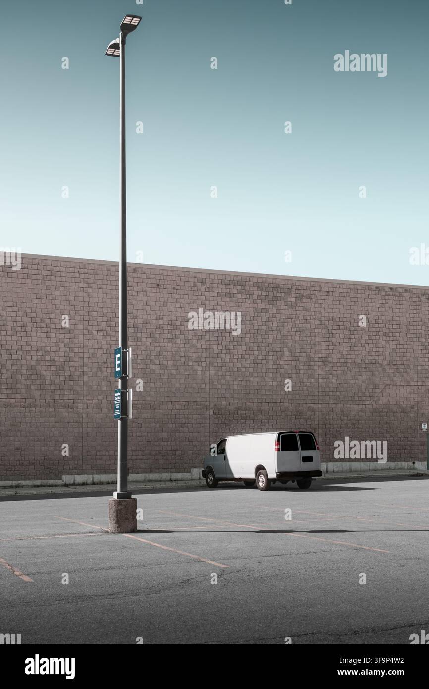 Camionnette de marchandises blanche garée à côté d'un grand lampadaire et d'un mur de briques sans fenêtre dans un parking vide à Kitchener, Ontario, Canada. Banque D'Images