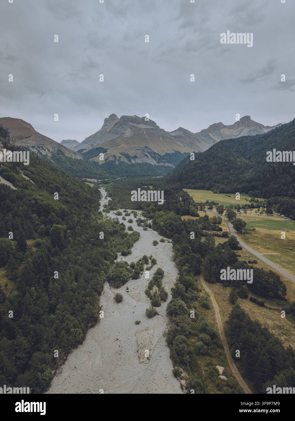 Vue aérienne du Vallon de la Jarjatte, présentant un lit de rivière sinueux, des forêts luxuriantes, des sommets montagneux et une route rurale sous un ciel nuageux à Lus-la-Cr Banque D'Images