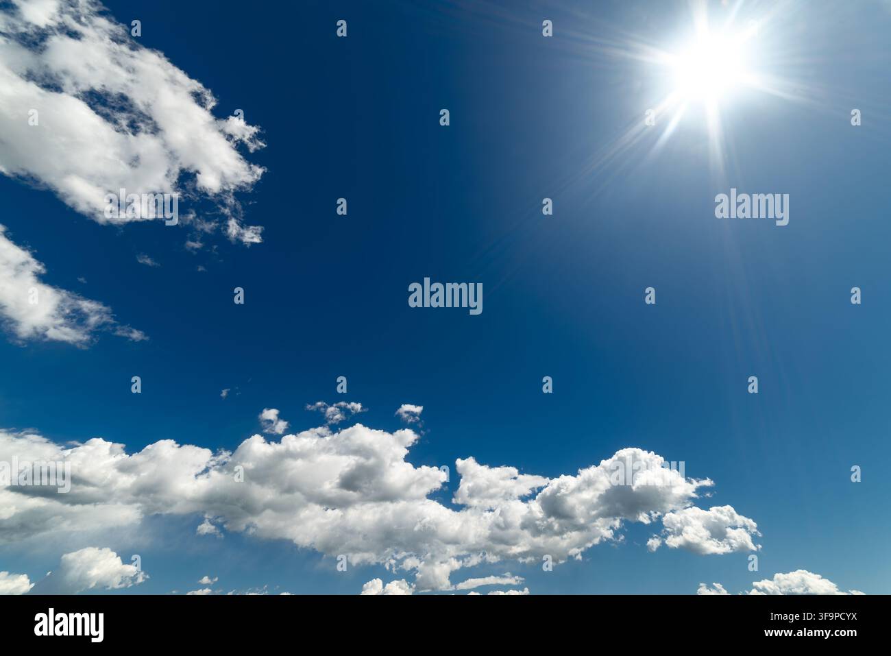 Journée ensoleillée et lumineuse avec un ciel bleu vif rempli de nuages cumulus blancs et duveteux. Le soleil radieux brille magnifiquement dans le coin supérieur, projetant Banque D'Images