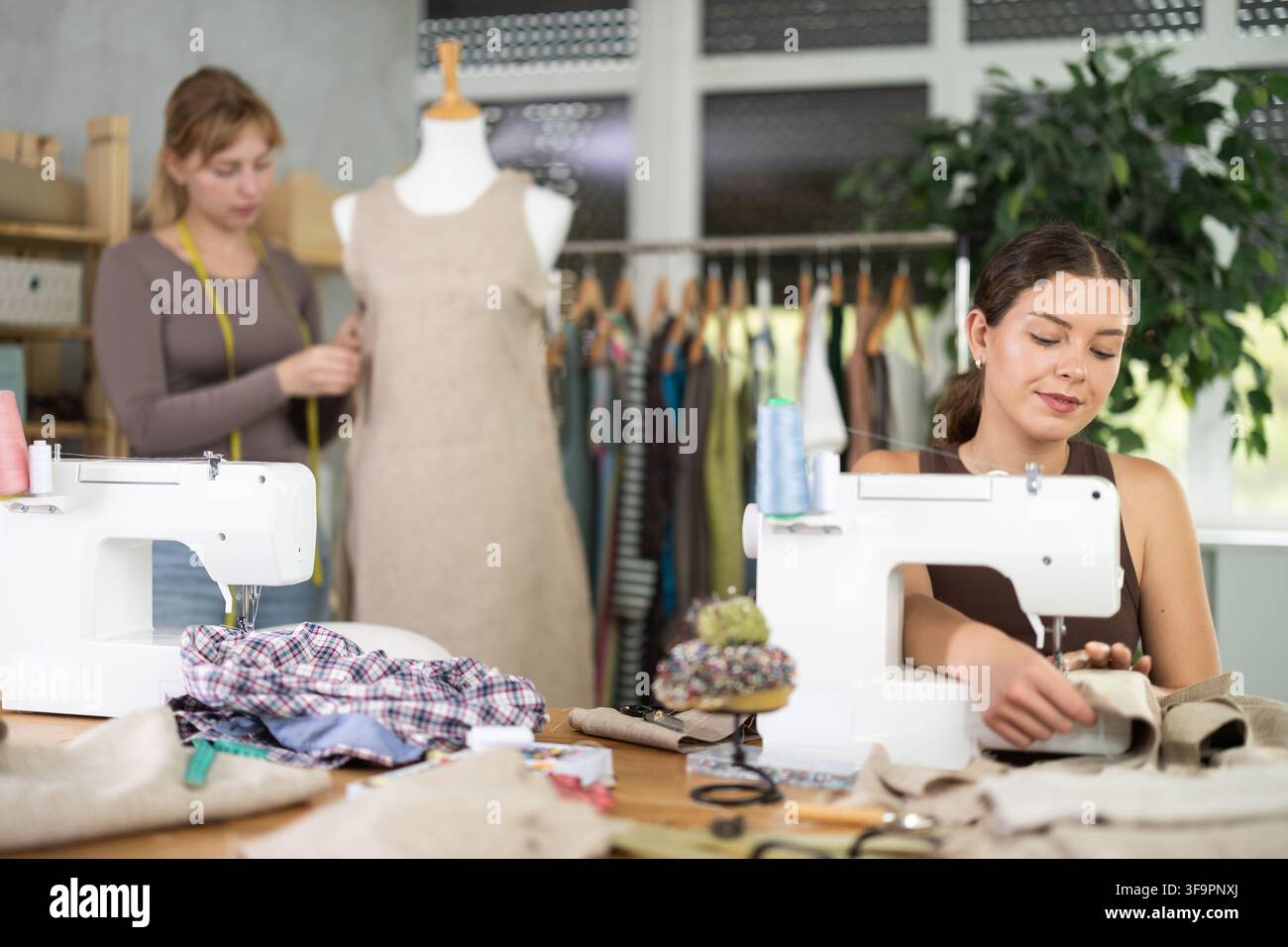 Tailleur femme travaillant sur une machine à coudre avec un assistant en arrière-plan Banque D'Images