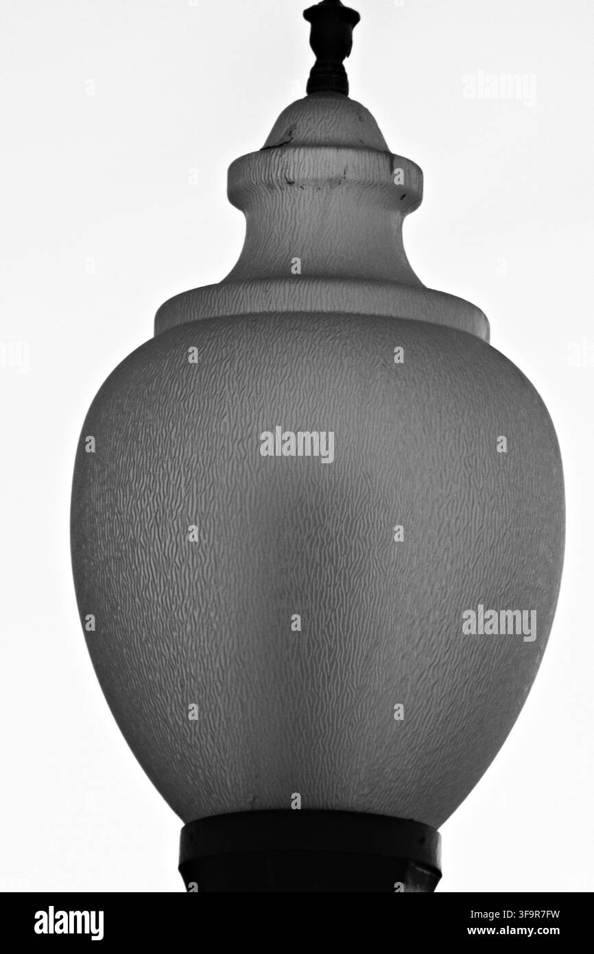 Lampe de rue classique au design orné et au verre texturé. Un éclairage doux met en valeur sa forme incurvée contre un ciel pâle. Adaptée à la conception urbaine, vintage Banque D'Images