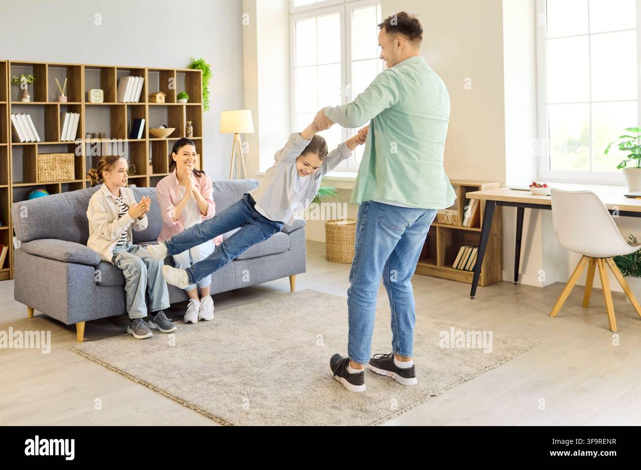 Père faisant tourner sa fille tandis que la famille acclame dans un salon lumineux et confortable à la maison Banque D'Images