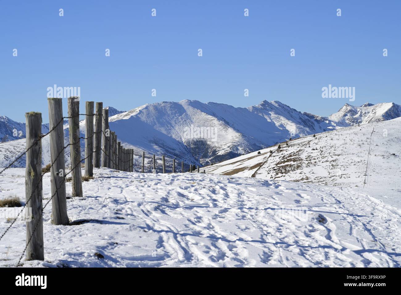 Panorama d'un paysage montagneux enneigé avec une clôture en bois à côté d'un sentier pour les skieurs de randonnée par une journée d'hiver claire Banque D'Images