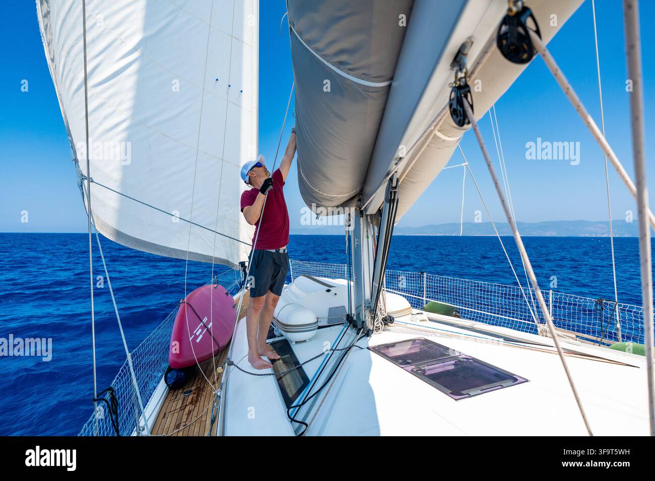 Homme ajustant la grand-voile sur un yacht à voile lors d'un voyage au large. Navigateur expérimenté ajustant la forme de la voile pour une propulsion éolienne efficace, en sécurité Banque D'Images