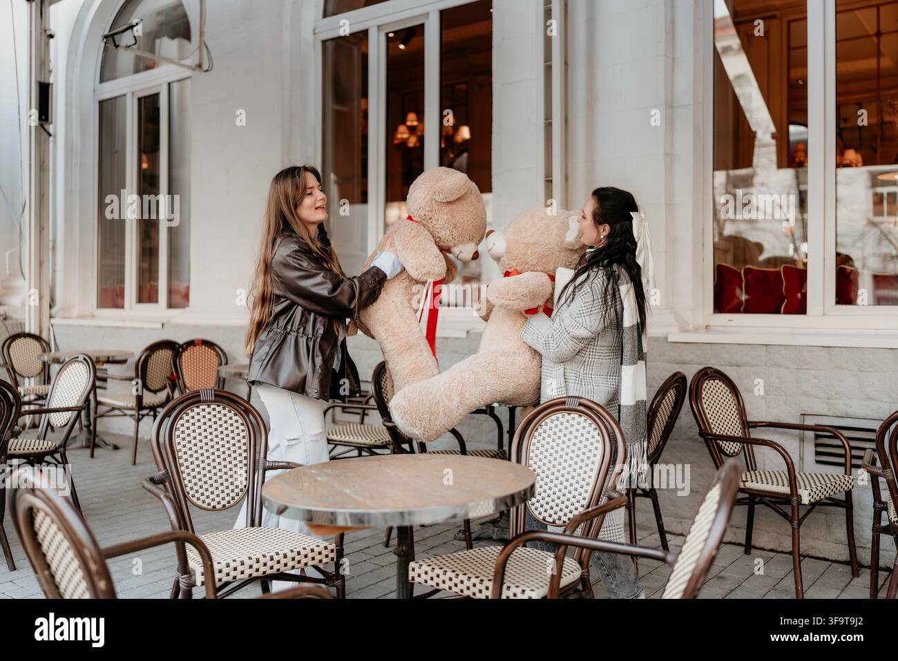 Café des amis avec des ours en peluche où deux jeunes femmes jouent avec des jouets en peluche sur une terrasse extérieure lors d'un après-midi de loisirs joyeux ensemble Banque D'Images