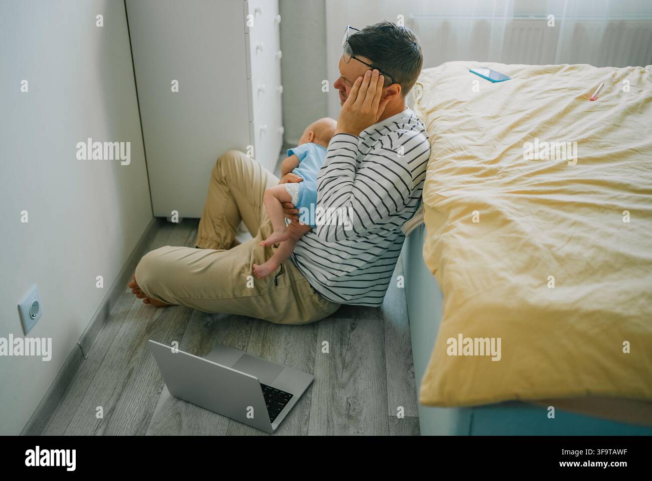 Père stressé subissant un épuisement émotionnel et des maux de tête en travaillant de chez lui, luttant avec les responsabilités parentales et un bébé qui pleure, se sentant submergé par les exigences familiales et professionnelles Banque D'Images