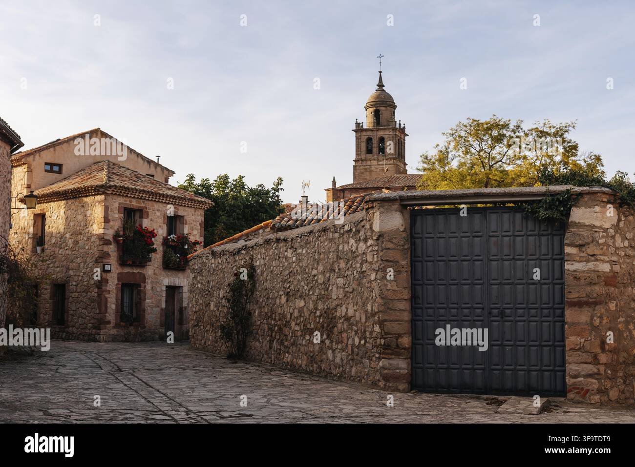 Rue du village de Medinaceli avec des maisons traditionnelles en pierre, un grand mur de pierre, une porte métallique et un clocher baroque Banque D'Images