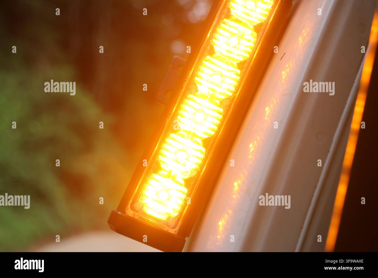 Une bande de diodes électroluminescentes jaune ambre sur une lumière de véhicule à côté d'un panneau de carrosserie blanc, gros plan avec lueur chaude et arrière-plan flou à l'extérieur Banque D'Images