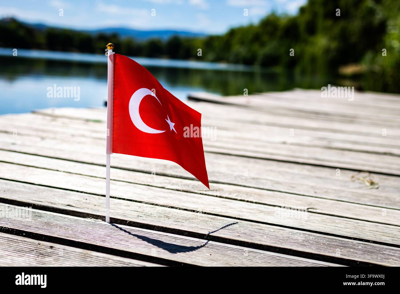 Petit drapeau de la Turquie montrant l'étoile et le croissant planté sur des planches de bois au bord d'un lac tranquille sous un ciel lumineux exprimant la fierté nationale, l'énergie du tourisme et Banque D'Images