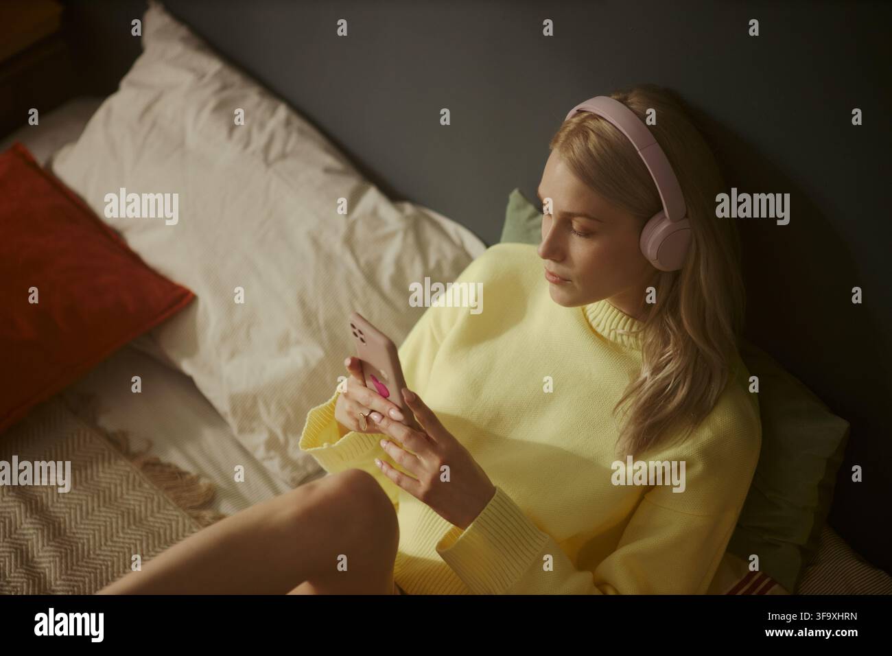 Jeune femme caucasienne portant des écouteurs et utilisant un smartphone allongée dans un lit. L'image représente le divertissement numérique et convient au marketing d'applications mobiles, vue en hauteur Banque D'Images