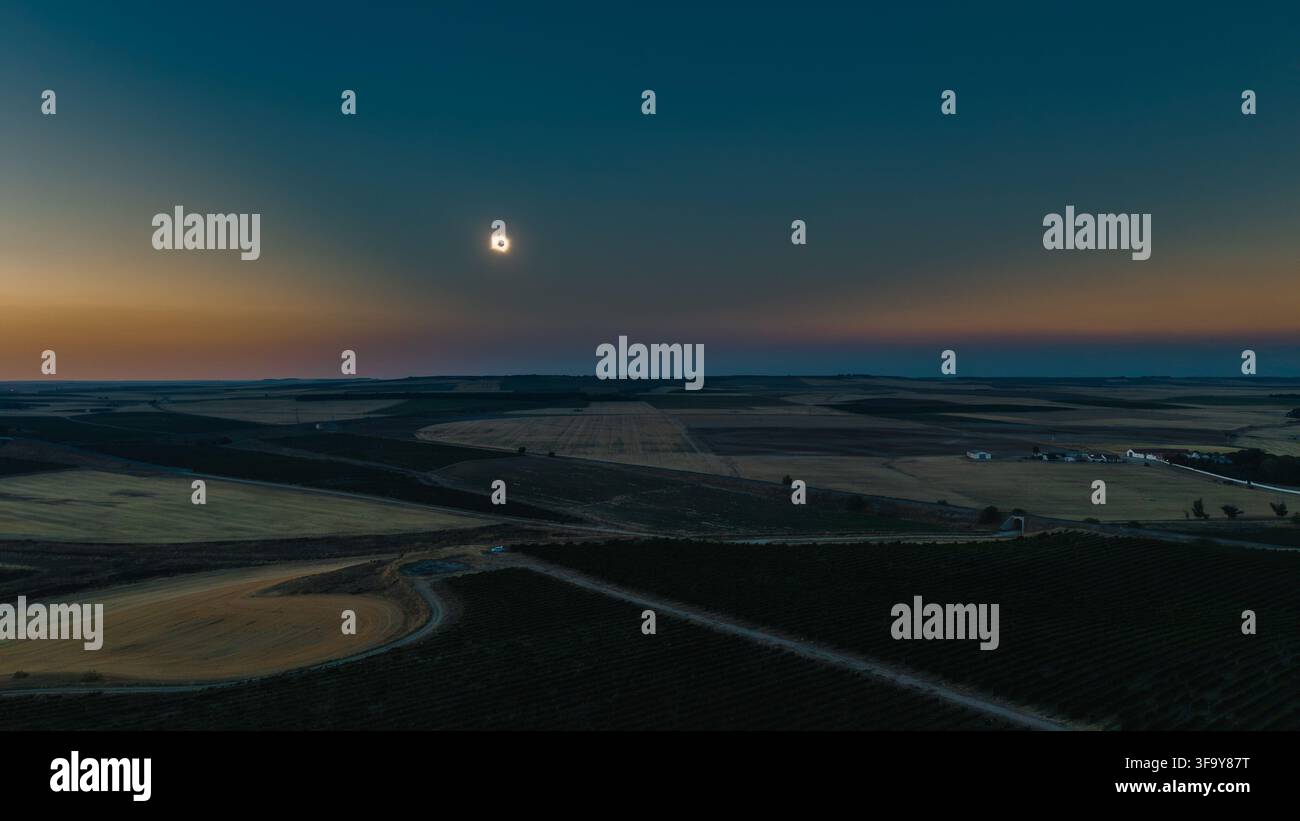 La lune occultant complètement le soleil, révélant la couronne solaire sous forme d'un anneau lumineux, projetant un crépuscule surnaturel sur des champs cultivés ondulants Banque D'Images