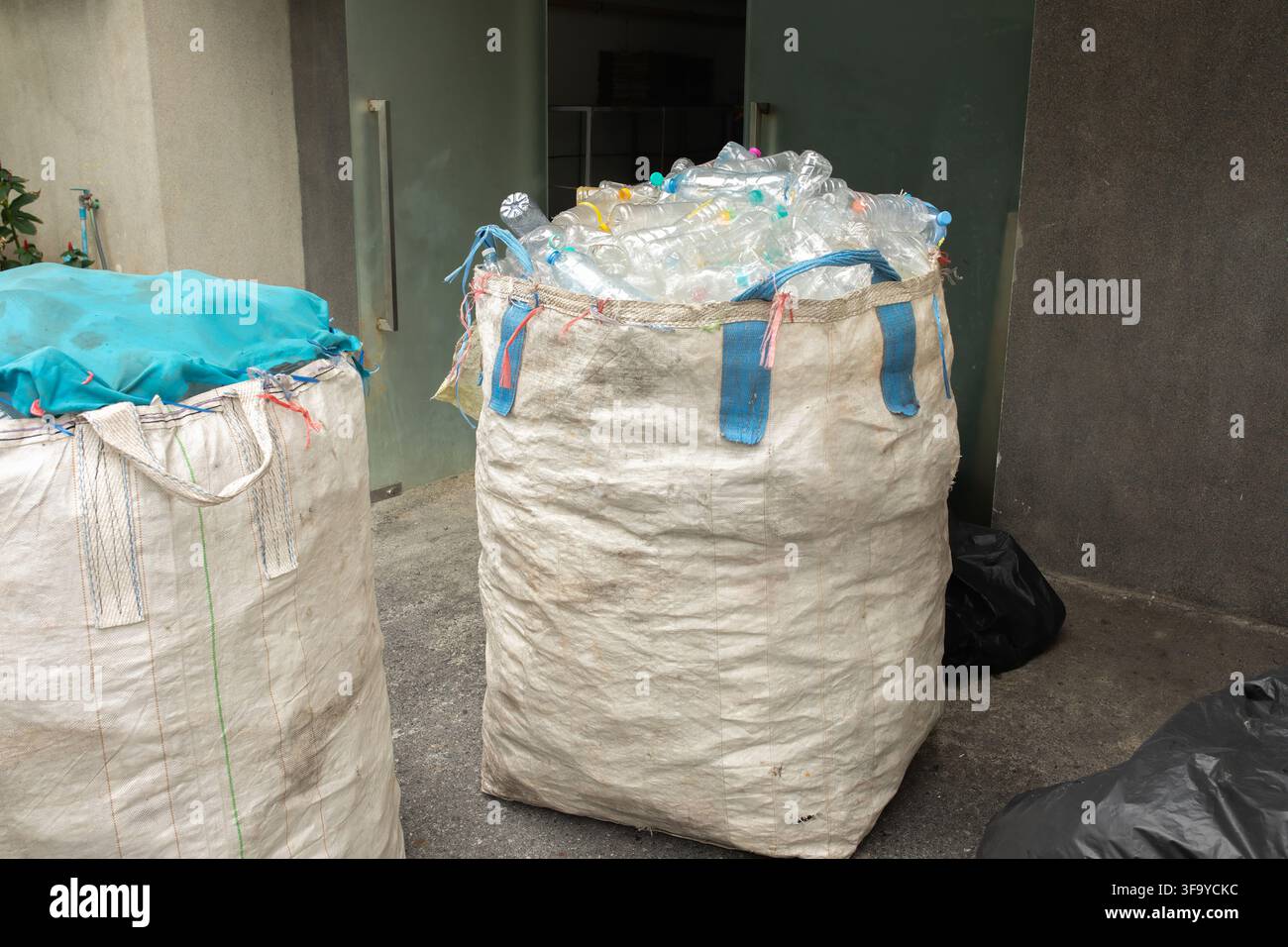Grands sacs tissés remplis de bouteilles en plastique transparent collectées pour le recyclage, concept de durabilité et de gestion des déchets dans une zone de stockage extérieure Banque D'Images