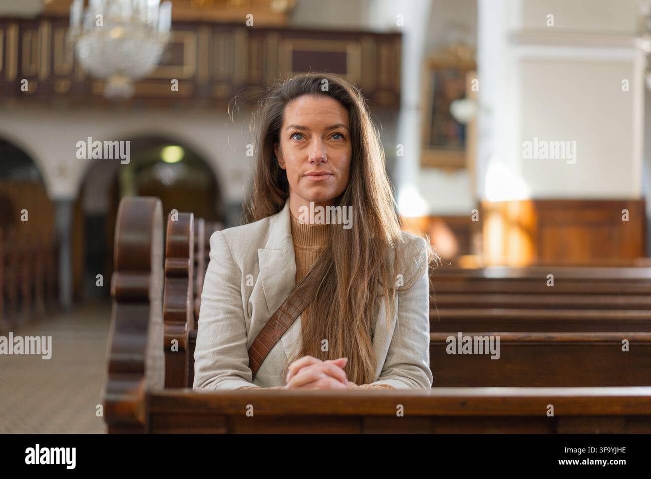 Une femme est assise dans une église, priant les mains jointes pendant la messe solennelle. Elle montre sa foi et sa dévotion. Banque D'Images
