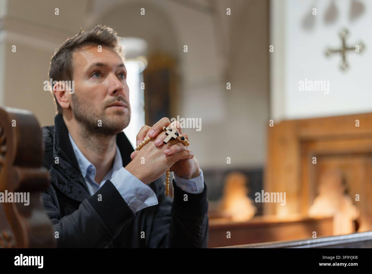 Un homme est assis dans une église catholique et prie pendant une sainte messe tout en montrant sa foi et sa dévotion. Le cadre est solennel et significatif. Banque D'Images