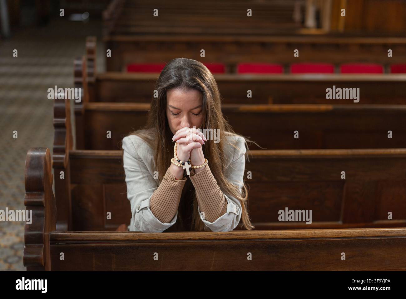 Une femme prie seule dans une église catholique européenne pendant la messe solennelle. Elle montre sa dévotion et sa foi par sa prière. Banque D'Images