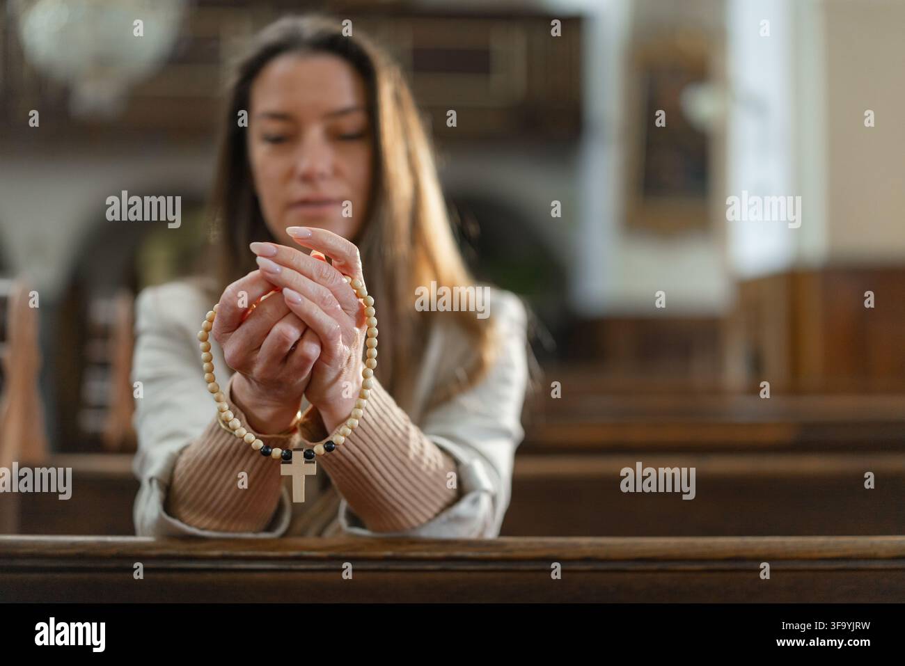 Une femme prie dans une église catholique européenne pendant la messe solennelle, montrant sa foi et sa dévotion. Elle tient un chapelet entre ses mains. Banque D'Images