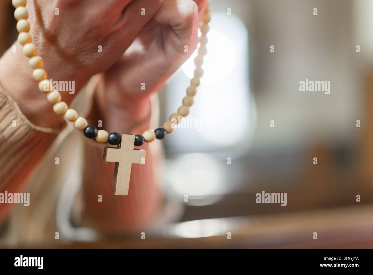 Une femme prie avec un chapelet dans une église catholique européenne pendant la messe solennelle. Elle montre sa foi et sa dévotion par cet acte. Banque D'Images