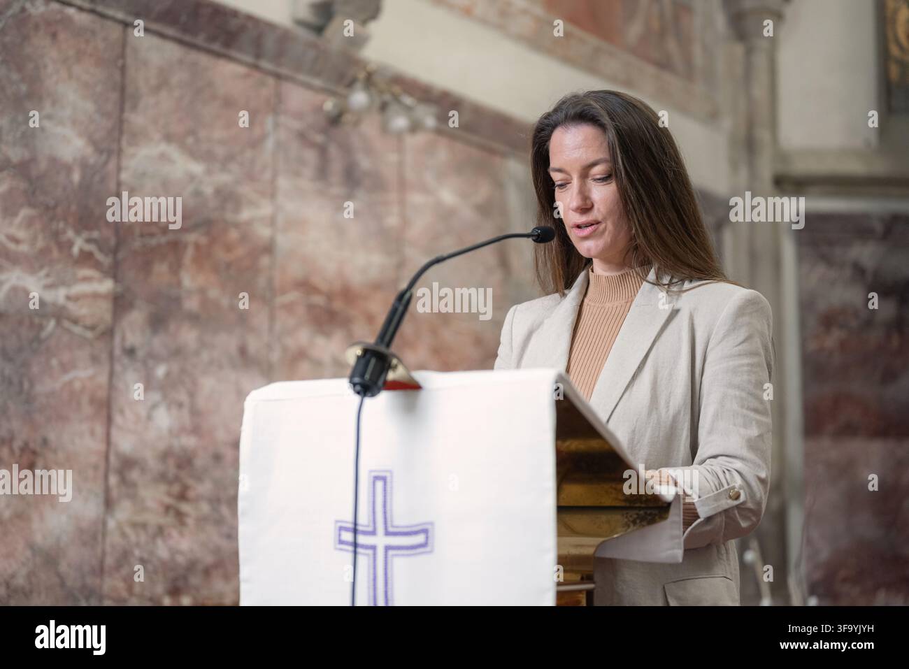 Femme chrétienne lisant dans une Bible à un lutrin lors d'une messe catholique dans une église européenne, concentrée sur les Écritures et l'adoration. Banque D'Images
