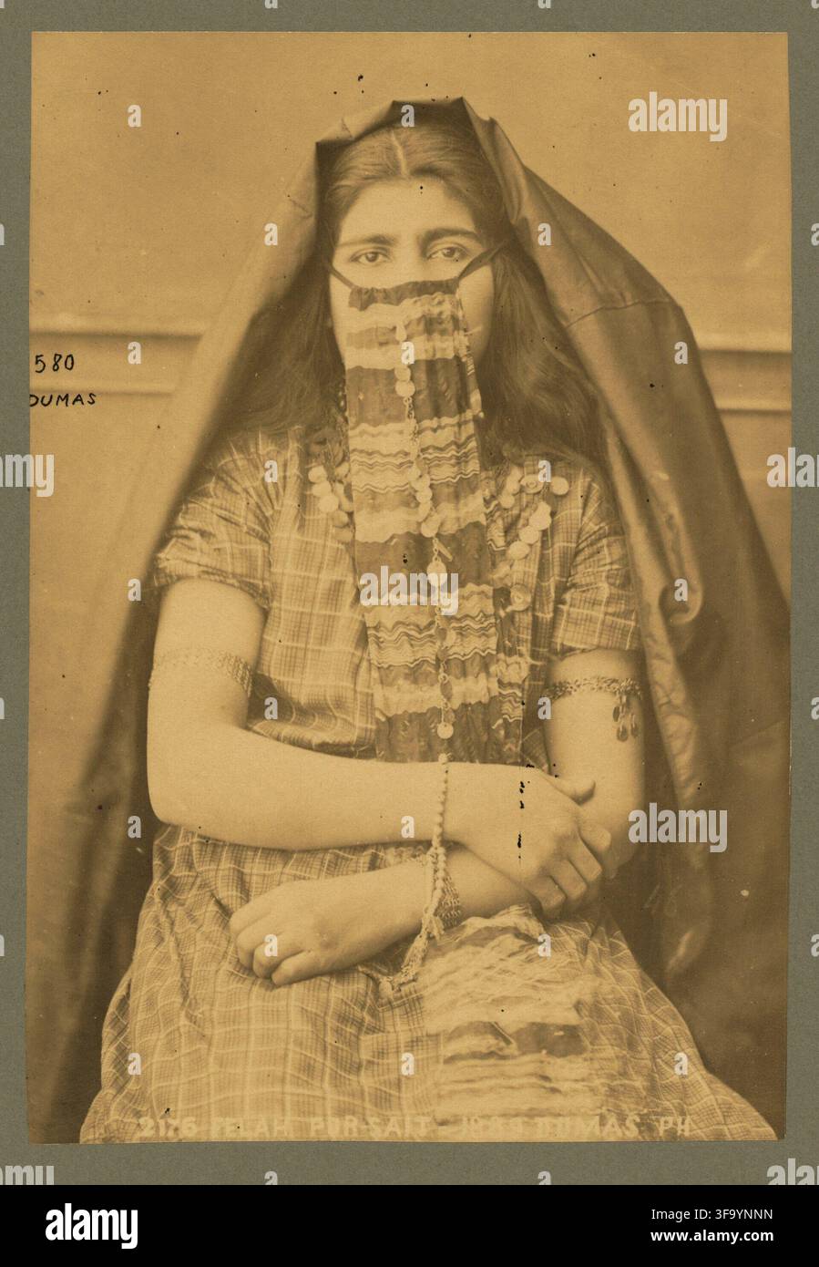 Portrait à l’albumine du XIXe siècle d’une jeune femme égyptienne assise à Port-Saïd, Égypte, photographiée en 1889 par Tancrède R. Dumas. Elle porte un voile, un ornement facial décoratif, des bijoux et une robe à motifs. Le titre français imprimé, « Felah Por-Sait », utilise une étiquette historique pour un paysan égyptien et une orthographe ancienne de Port-Saïd ; il n’identifie pas personnellement la personne non nommée. Banque D'Images