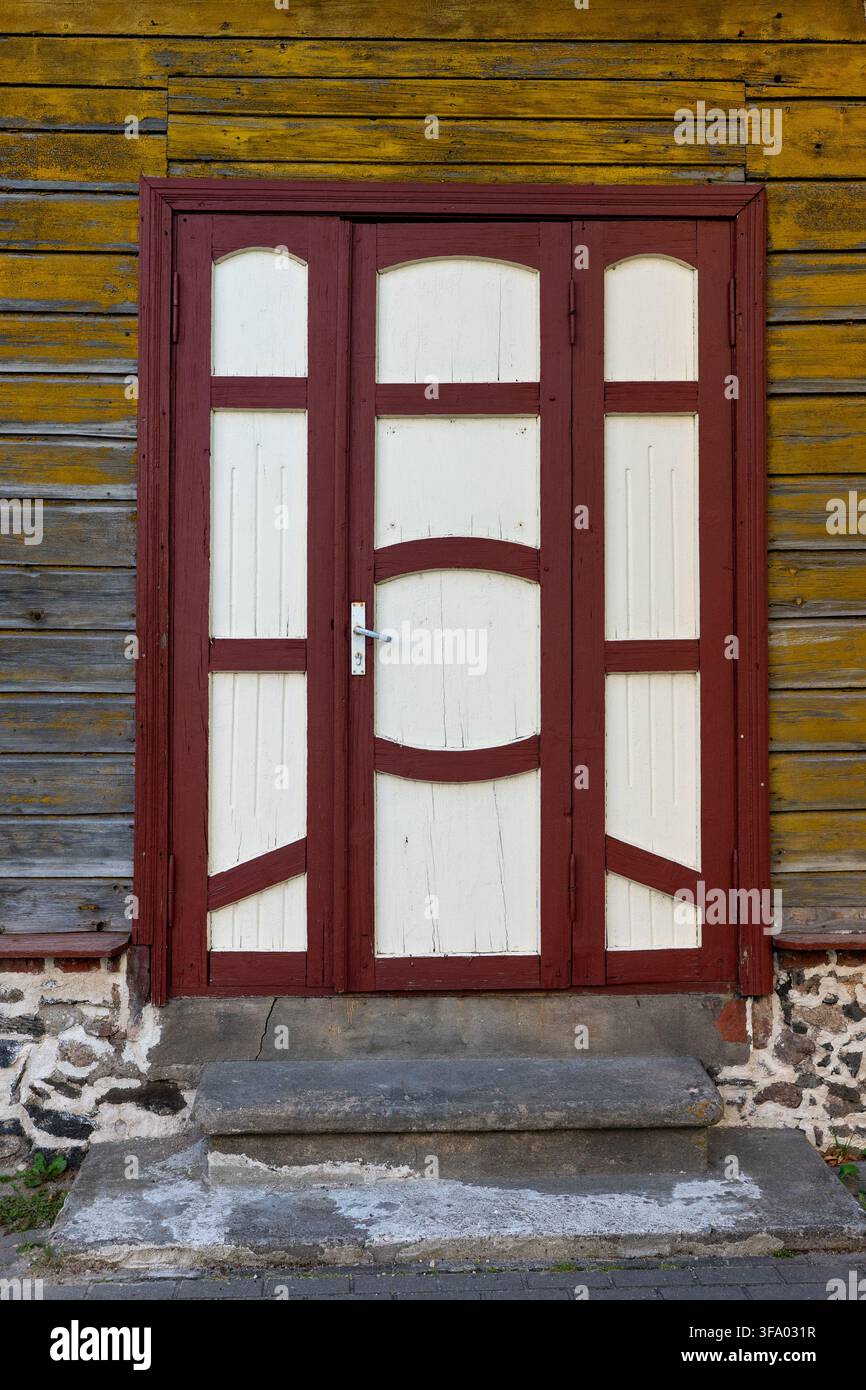 Porte d'entrée traditionnelle en bois vieilli avec des panneaux bordeaux et crème dans une façade en bois vieilli à Võru, en Estonie. Banque D'Images