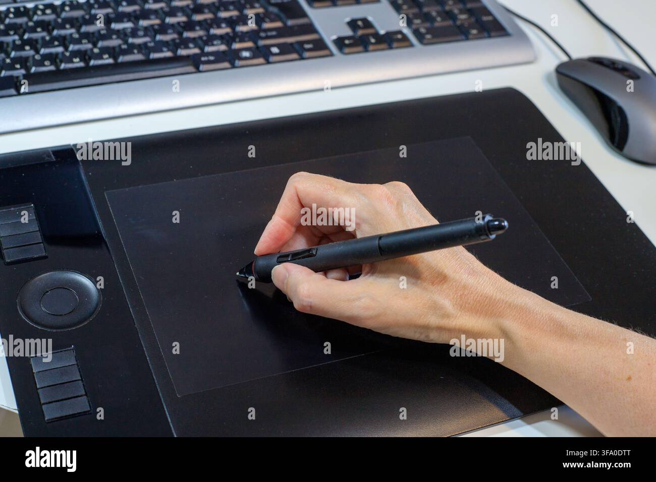 La main du designer dessine avec un stylet numérique sur une tablette graphique noire posée sur un bureau à côté d'un clavier d'ordinateur. Processus créatif d'un illustrateur numérique Banque D'Images
