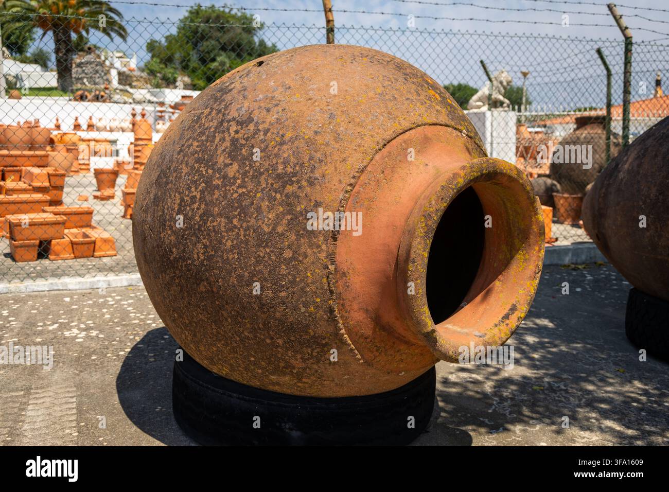 Une grande amphore en terre cuite, vieille et érodée, est exposée à l'extérieur, peut-être sur un marché ou dans un magasin de jardinage, avec d'autres poteries en arrière-plan Banque D'Images