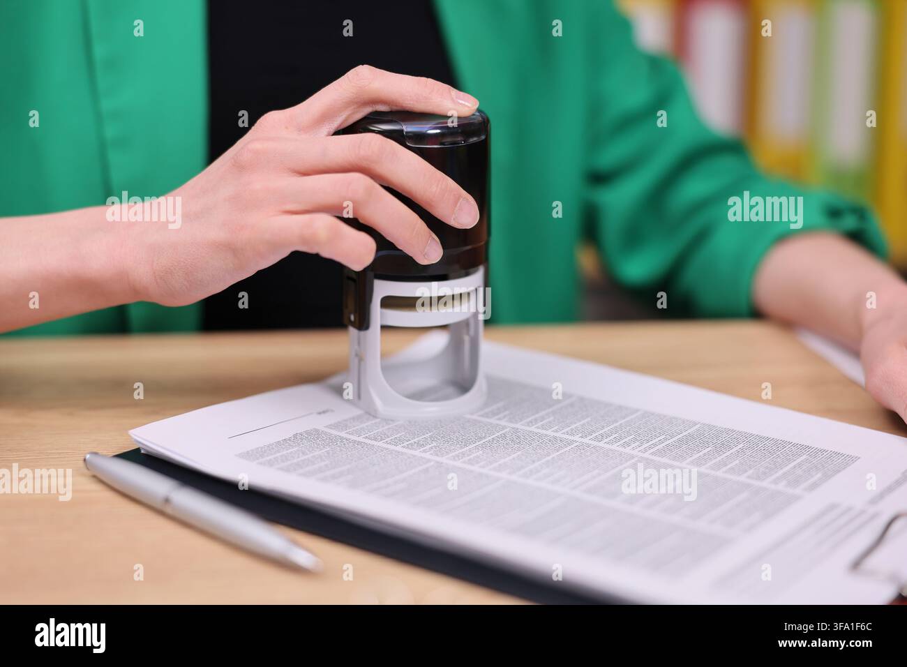 Main appuyant un tampon auto-encreur sur des documents sur un bureau avec un arrière-plan de bureau flou, vue rapprochée de l'approbation du document, administration de bureau, dossier Banque D'Images