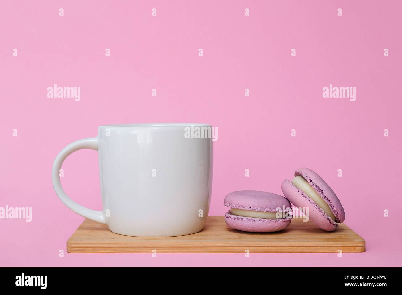Macarons français roses et tasse en céramique blanche sur fond rose uni, pause de nature morte douce et chaleureuse. Banque D'Images