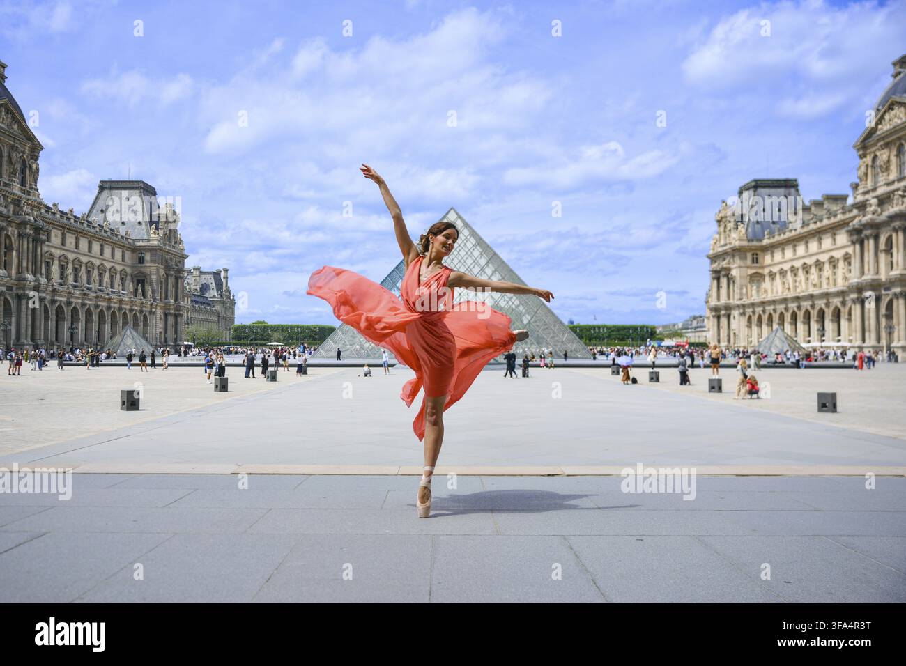 Femme gracieuse dansant en robe rouge près de la pyramide du Louvre à Paris, France Banque D'Images