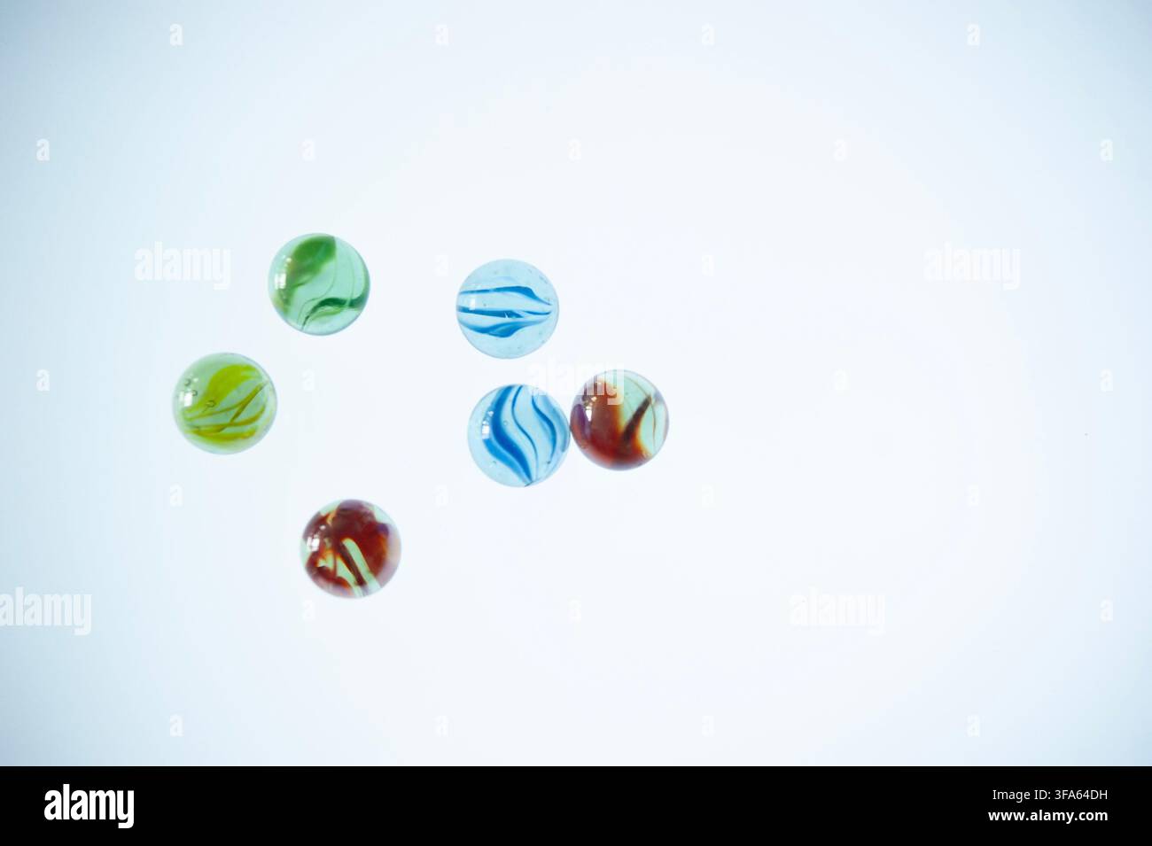 ix billes en verre colorées dispersées sur un fond blanc propre avec un espace de copie généreux, vues de dessus Banque D'Images