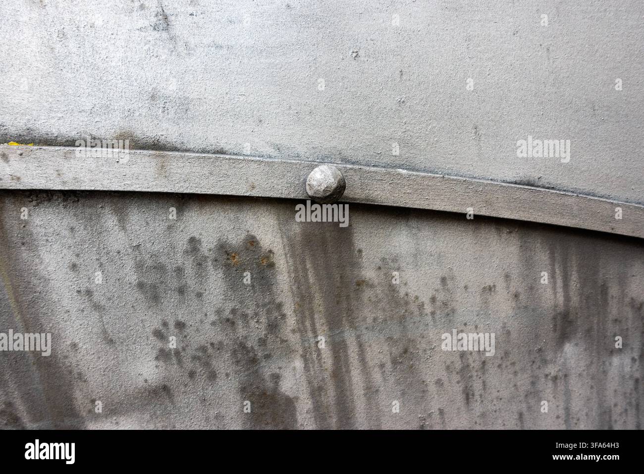 Gros plan d'une surface métallique grise usée avec un rivet rond, des taches sombres, des rayures et une texture de crasse industrielle Banque D'Images