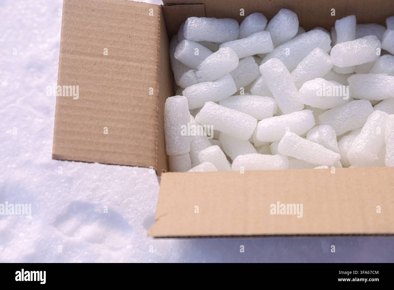 Une boîte en carton remplie de billes d'emballage en polystyrène blanc repose sur un sol enneigé blanc. Les objets sont nets et détaillés avec beaucoup d'espace pour le texte Banque D'Images