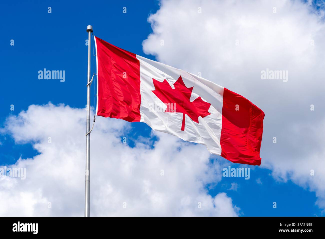 Un drapeau national du Canada flottant contre un ciel bleu parsemé de nuages blancs. Banque D'Images