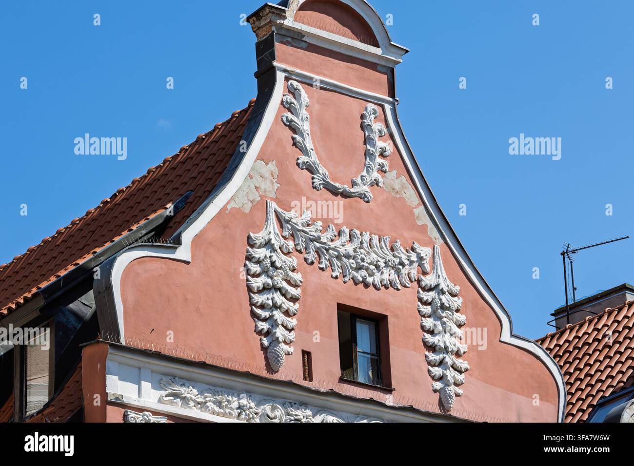Une maison de ville baroque à façade pastel présente des décorations en stuc ornées et un pignon à gradins typique de la vieille ville de Torun. Motifs floraux blancs Banque D'Images