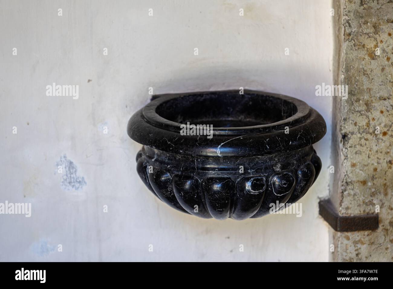 Un bénitier en marbre sombre est fixé à un mur intérieur d'église. Le bassin arrondi avec une cannelure décorative sculptée Banque D'Images