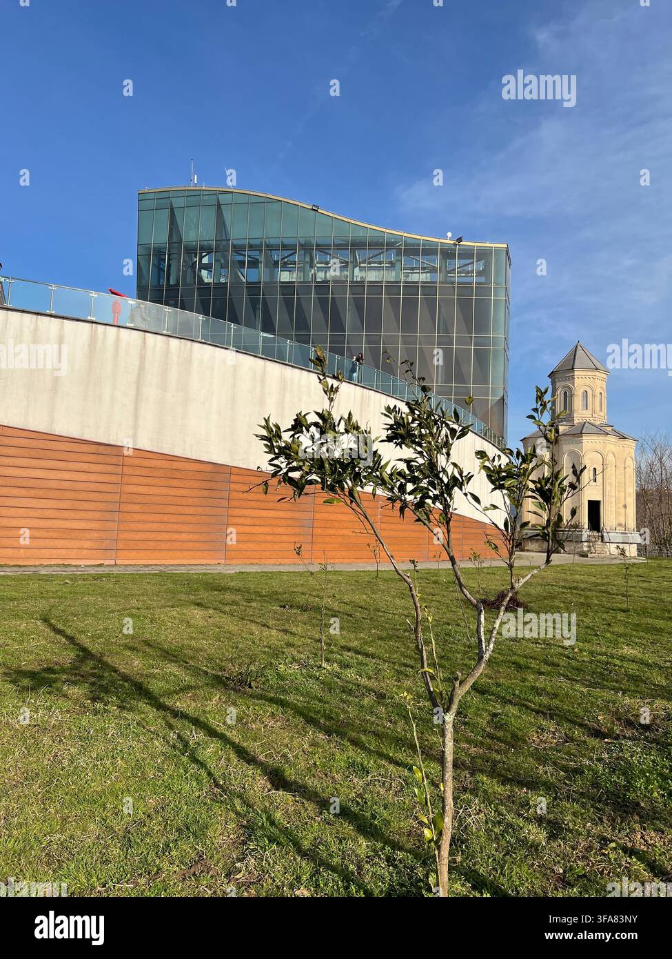 Bâtiment moderne en verre à côté d'un vieux clocher en pierre sur une pelouse verte. - Image de stock capturée avec un smartphone