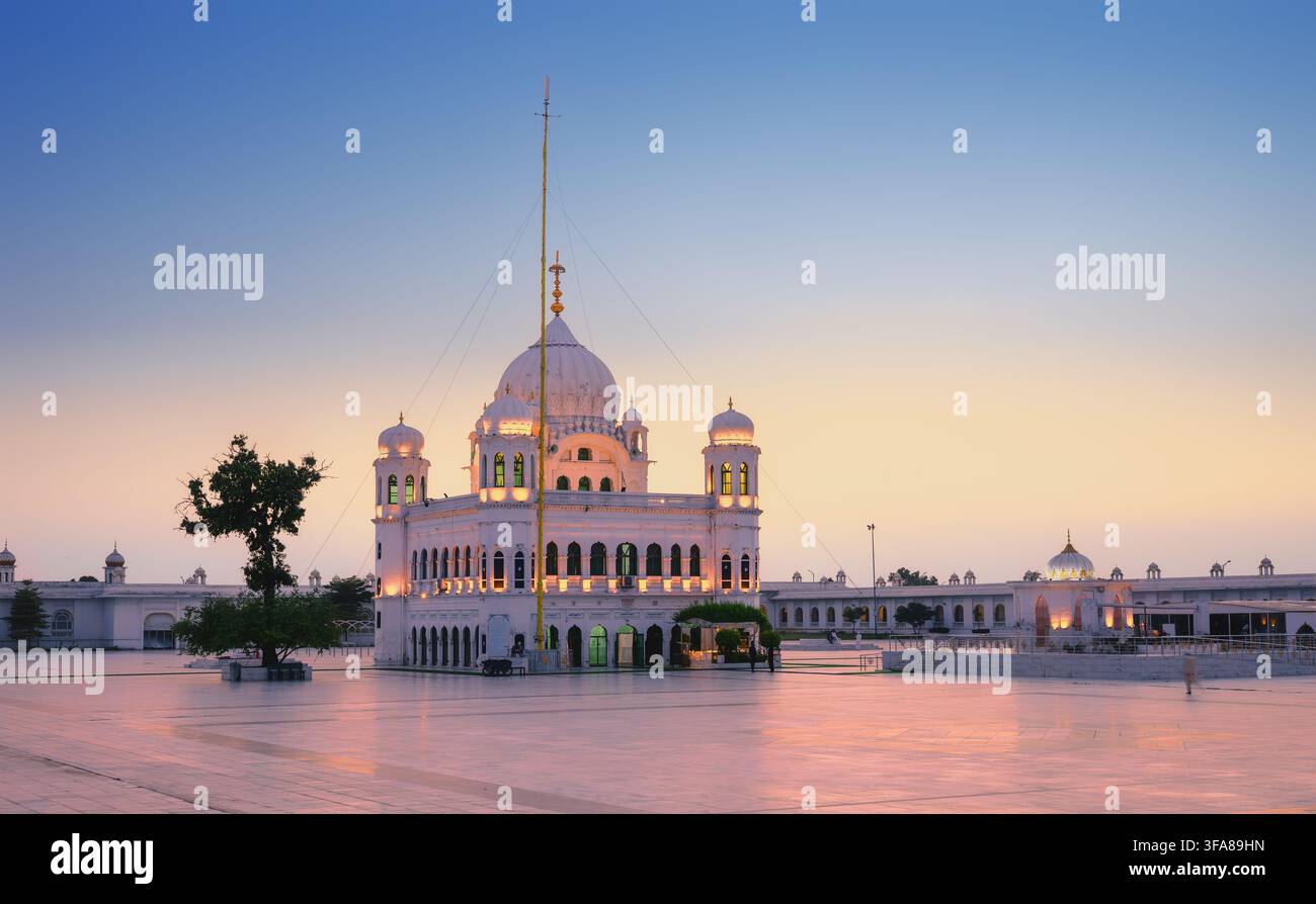 Vue de la structure en marbre blanc du Gurdwara Darbar Sahib Kartarpur au coucher du soleil, mettant en évidence sa coupole proéminente, son grand mât de drapeau et sa vaste cour pavée Banque D'Images