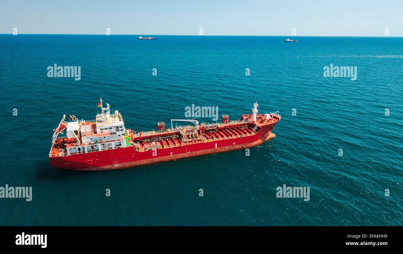 Vue aérienne d'un pétrolier rouge ancré dans une mer bleue calme avec des cargos distants Banque D'Images