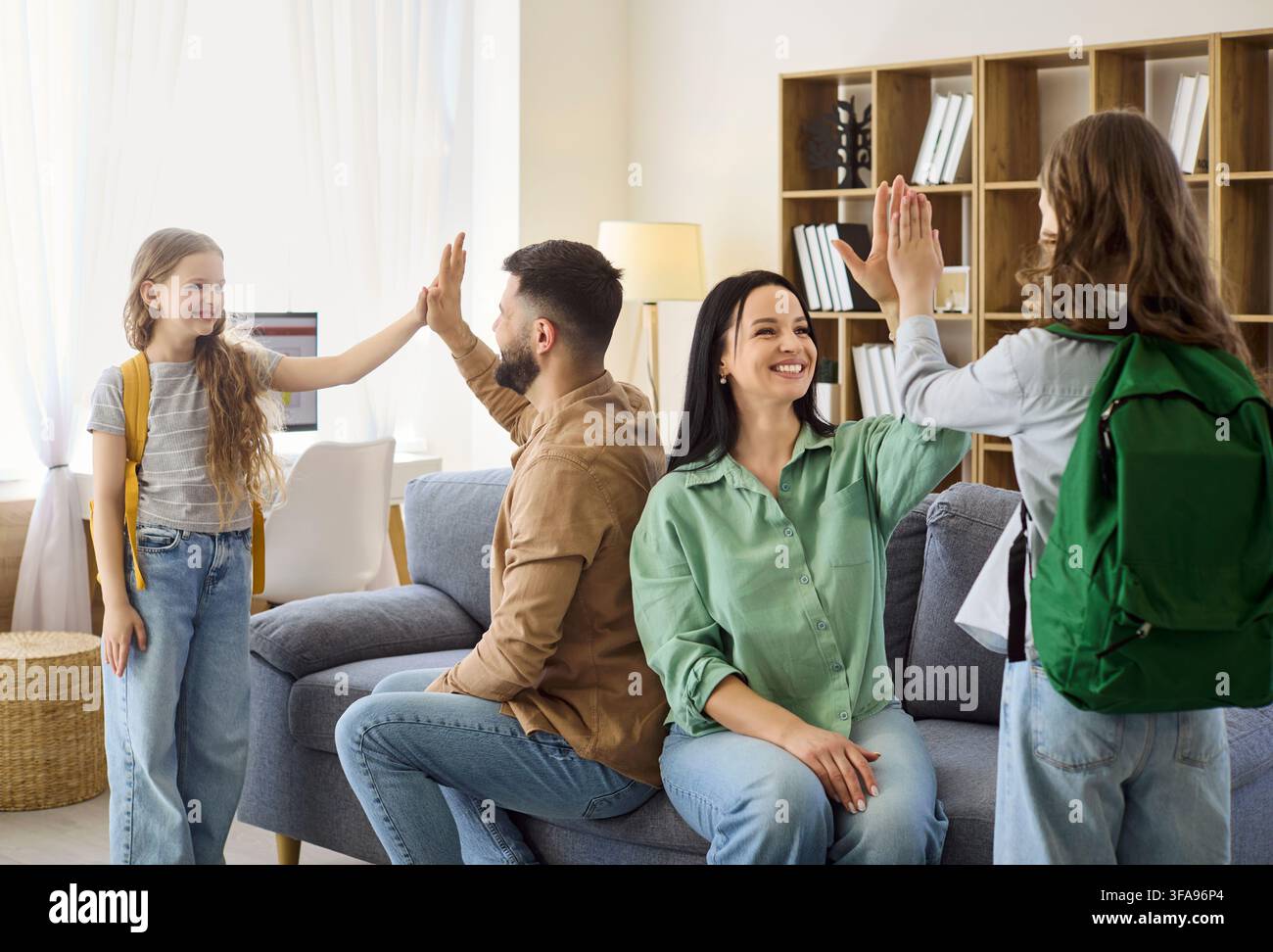Parents donnent un high five à leurs filles avec des sacs à dos avant l'école dans un salon confortable à la maison Banque D'Images