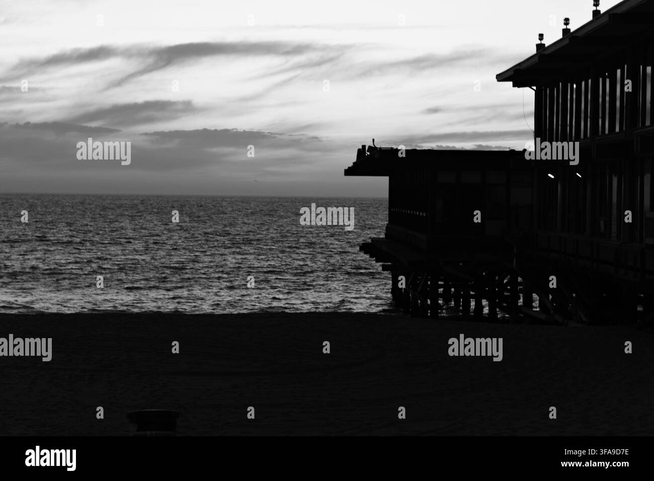 Le coucher de soleil peint l'océan dans des teintes chaudes. Les silhouettes de la jetée s'étendent sur les eaux calmes. Les dégradés du ciel mélangent orange, rose et bleu doux. Scène de plage paisible evo Banque D'Images