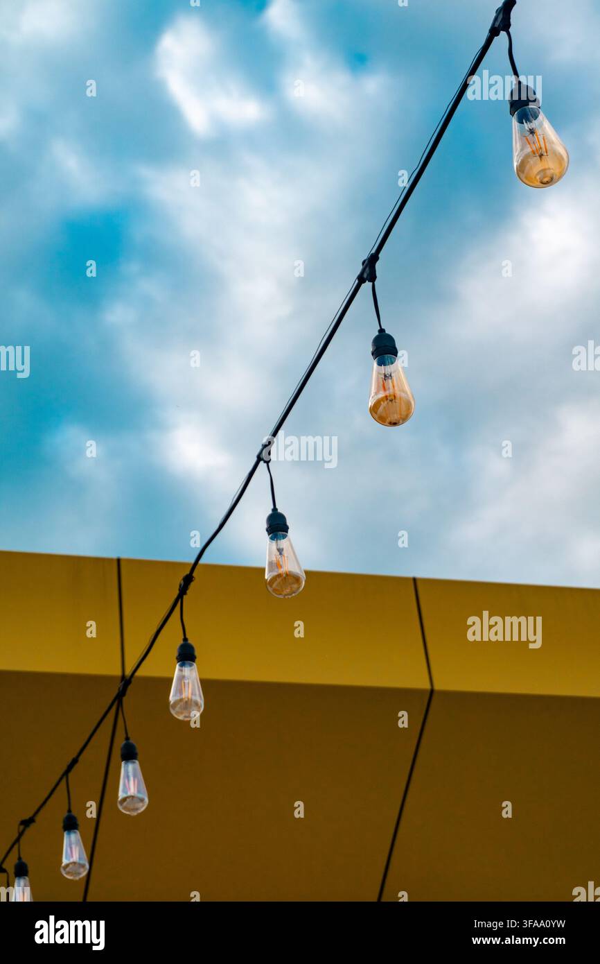 Guirlandes lumineuses décoratives suspendues contre un ciel bleu et un mur jaune d'immeuble. Banque D'Images