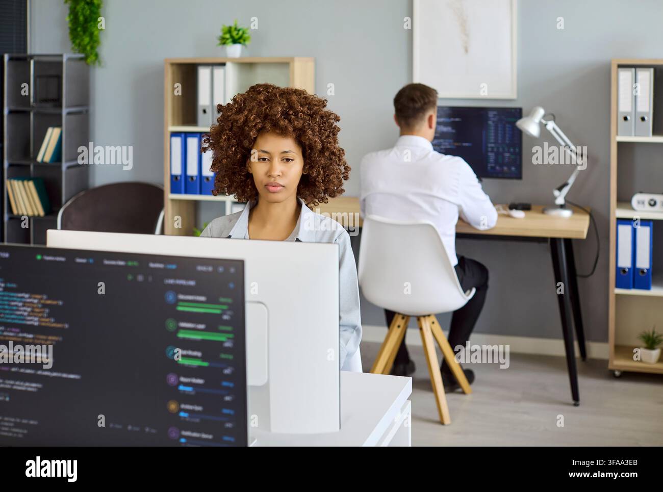 Développeurs codant des logiciels dans un bureau moderne avec moniteurs et collaboration d'équipe Banque D'Images