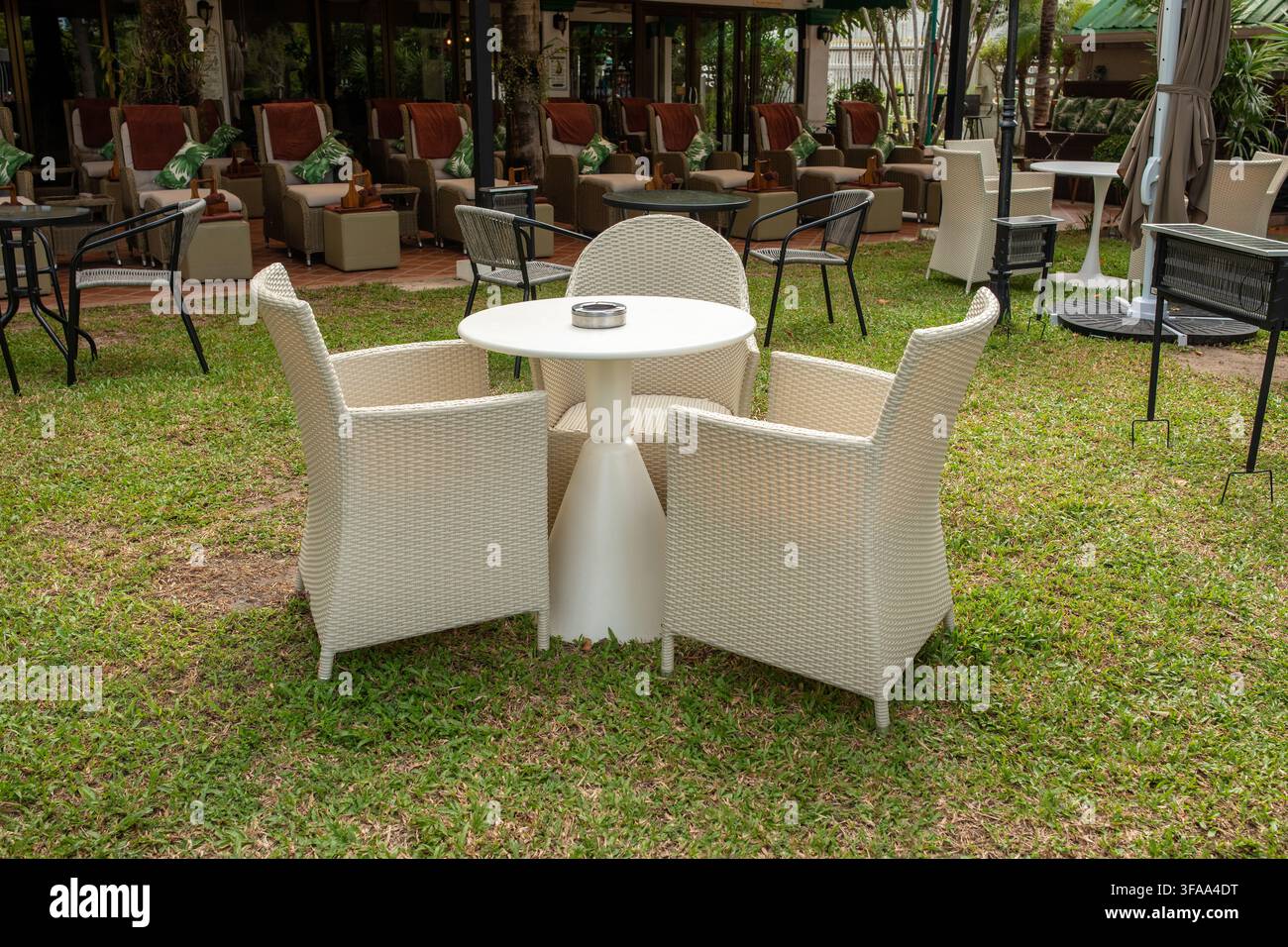 Table ronde d'extérieur avec chaises en rotin sur de la fausse pelouse verte dans un espace spa ou de massage en plein air, concept de salon de détente Banque D'Images