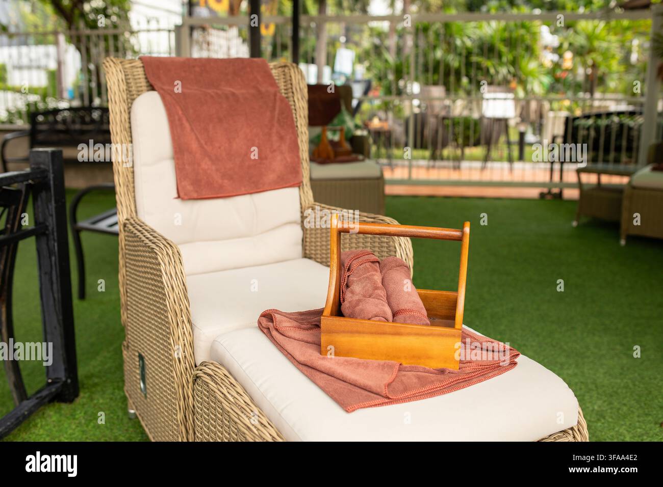 Gros plan d'une chaise de massage en osier avec panier en bois et serviettes sur de la pelouse artificielle verte en plein air, Thaïlande Banque D'Images