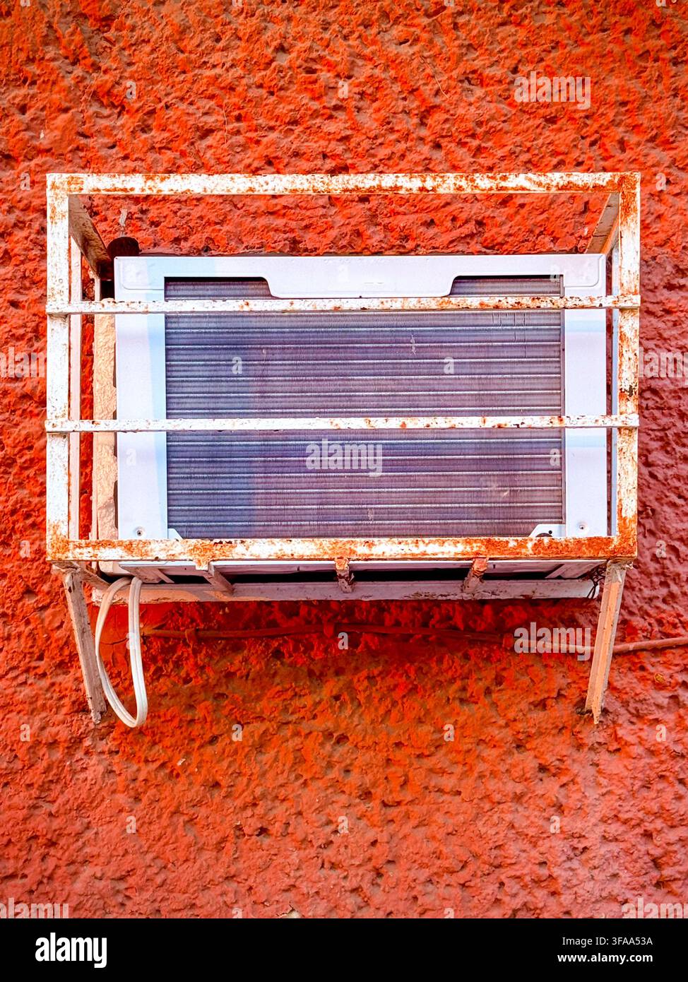 Une ancienne unité de climatisation murale dans une cage métallique de protection sur un mur lumineux à Mérida, au Mexique, illustrant la demande de refroidissement et la chaleur extrême Banque D'Images