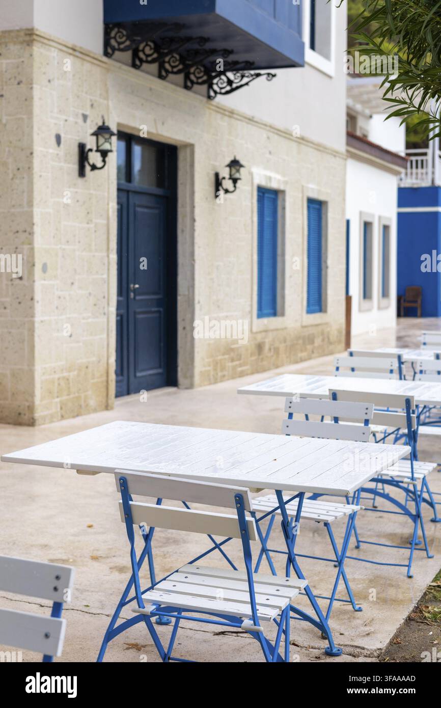Tables et chaises bleues et blanches disposées soigneusement dans une salle à manger extérieure agrémentée de touches bleues et de meubles blancs. Parfait pour savourer un repas à l'extérieur Banque D'Images