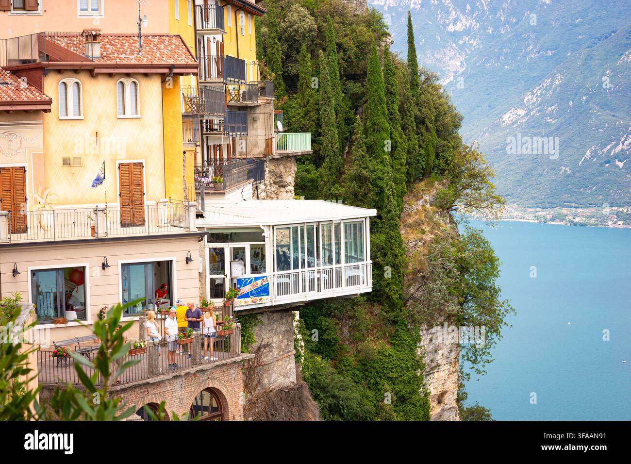 Balcon d'un restaurant au bord des falaises avec des touristes surplombant le lac de Garde et le paysage montagneux, Pieve, Italie. Banque D'Images