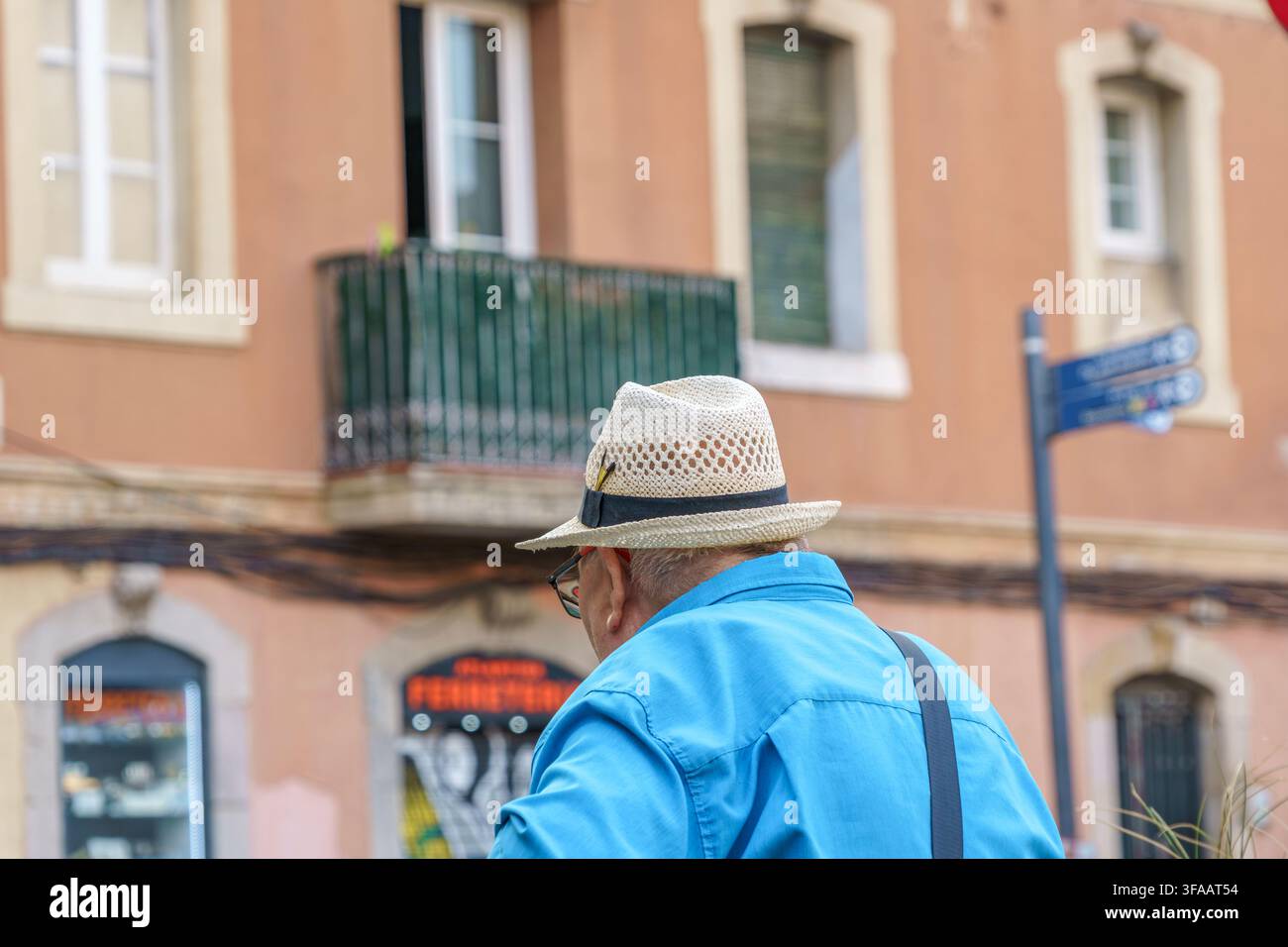 Barcelone – Espagne – 1er août 2026 : Homme âgé portant un chapeau de paille et une chemise bleue marchant dans une rue de ville européenne, touriste âgé, style de vie estival Banque D'Images
