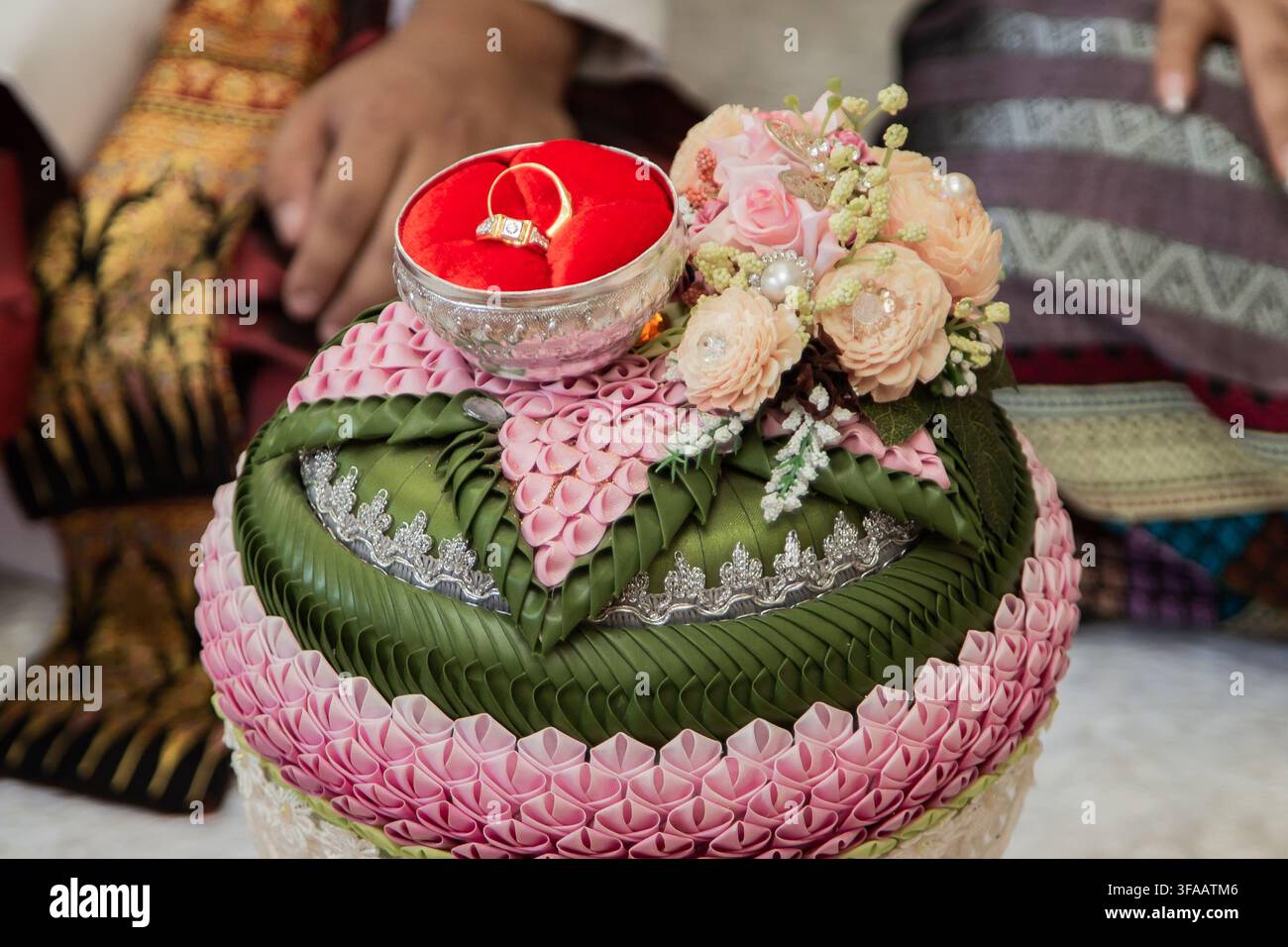 Plateau de fiançailles thaïlandais traditionnel décoré de feuilles vertes pliées et de fleurs roses contenant une bague en or dans un bol en velours rouge. Banque D'Images